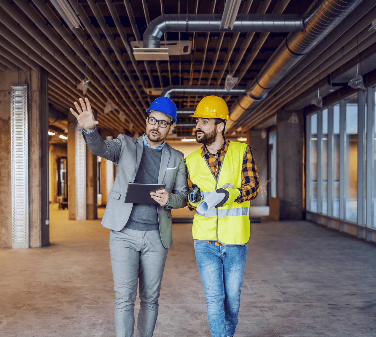 A project manager and a construction worker discuss plans in a partially finished commercial space, highlighting teamwork and project oversight.